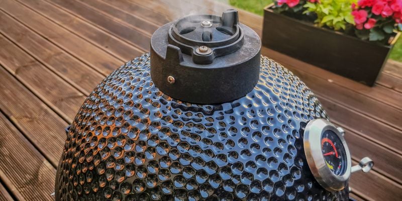The top of a kamado grill, a domed shaped grill, with steam coming out through holes.