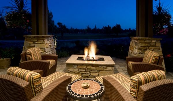 A backyard fire pit is lit while 4 chairs surround the space at twilight